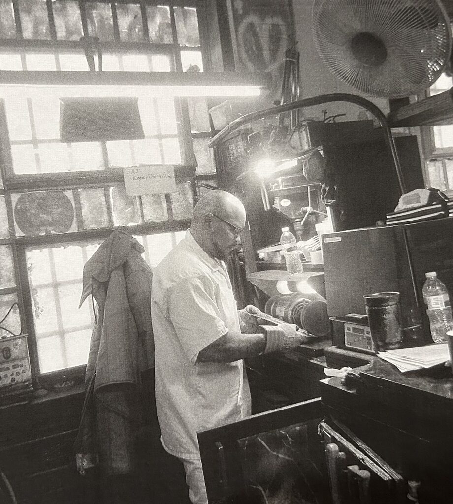 Black-and-white photo of Nanon working at a buffing wheel in the prison craft shop.