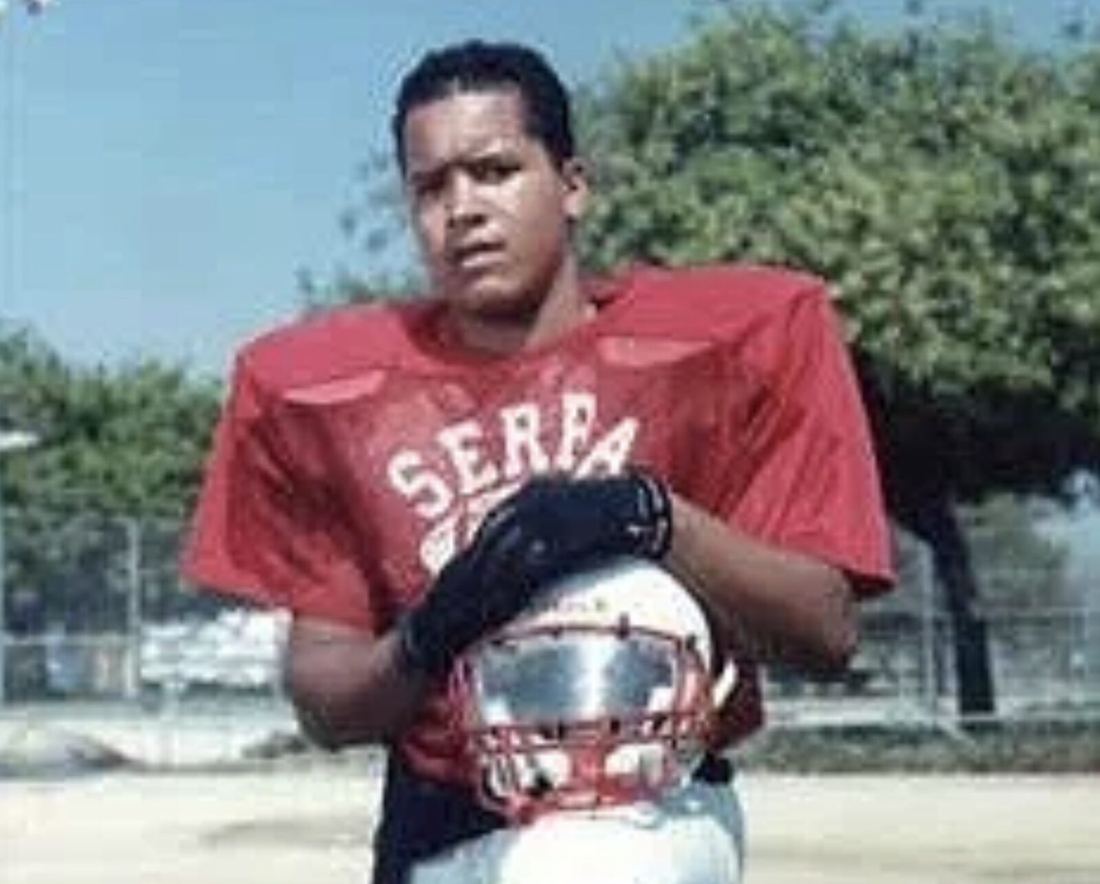 Nanon as a teenager in a red Serra football jersey, holding his helmet.