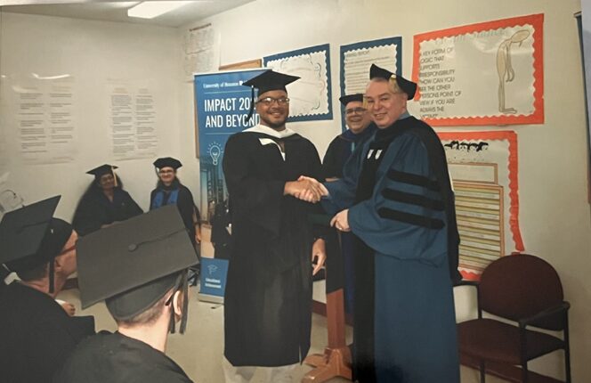 Nanon shaking hands with a faculty member in academic robes at his graduation ceremony.