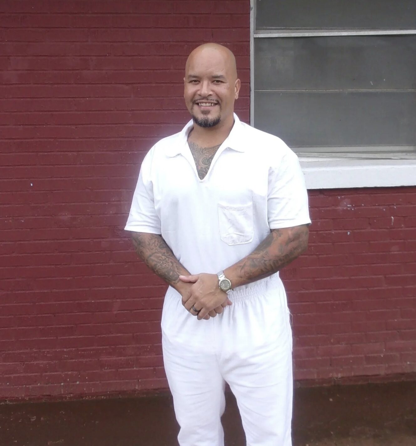 Nanon smiling in prison whites in front of a red brick wall.